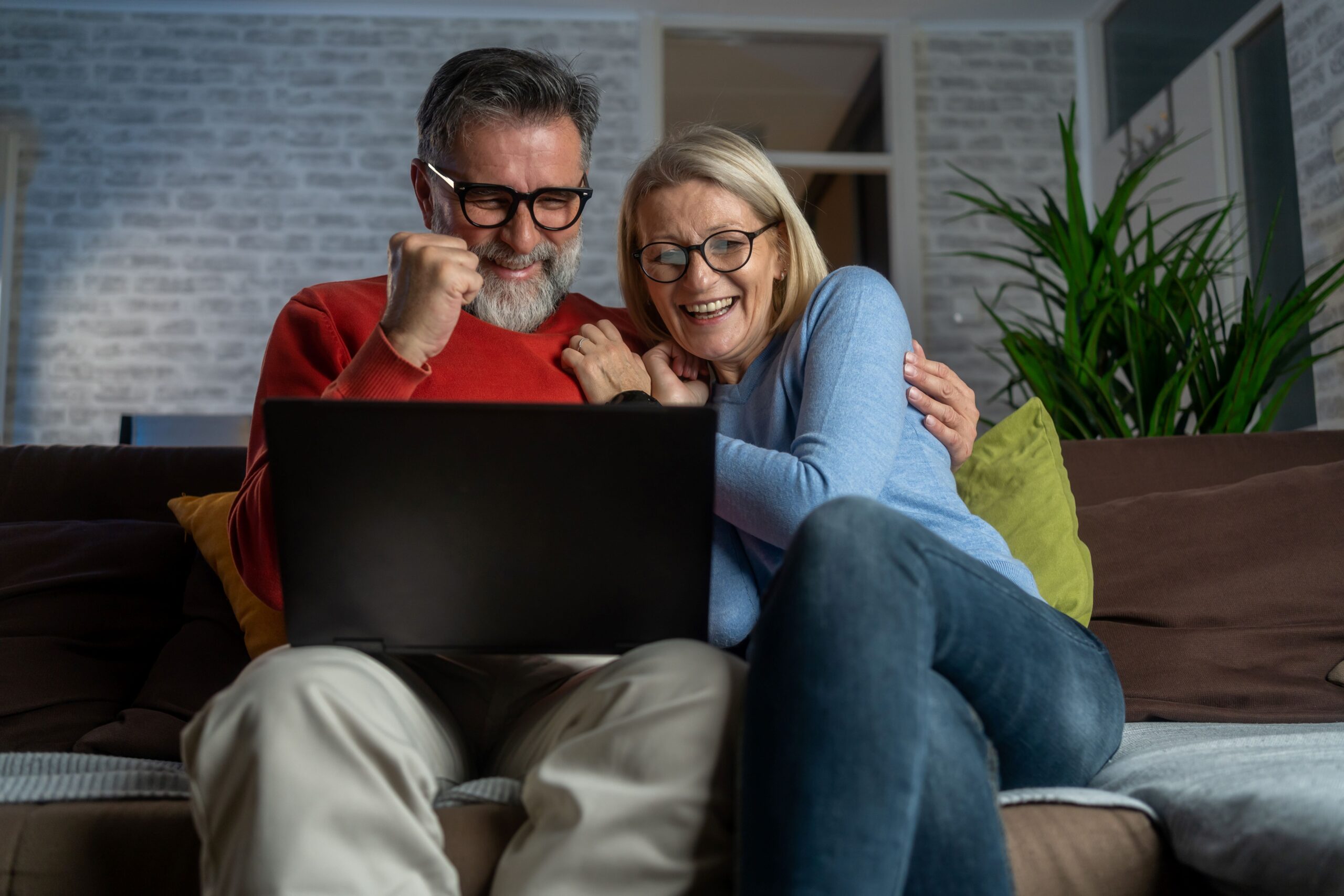 Ein Mann und eine Frau sitzen vor einem Laptop und freuen sich 